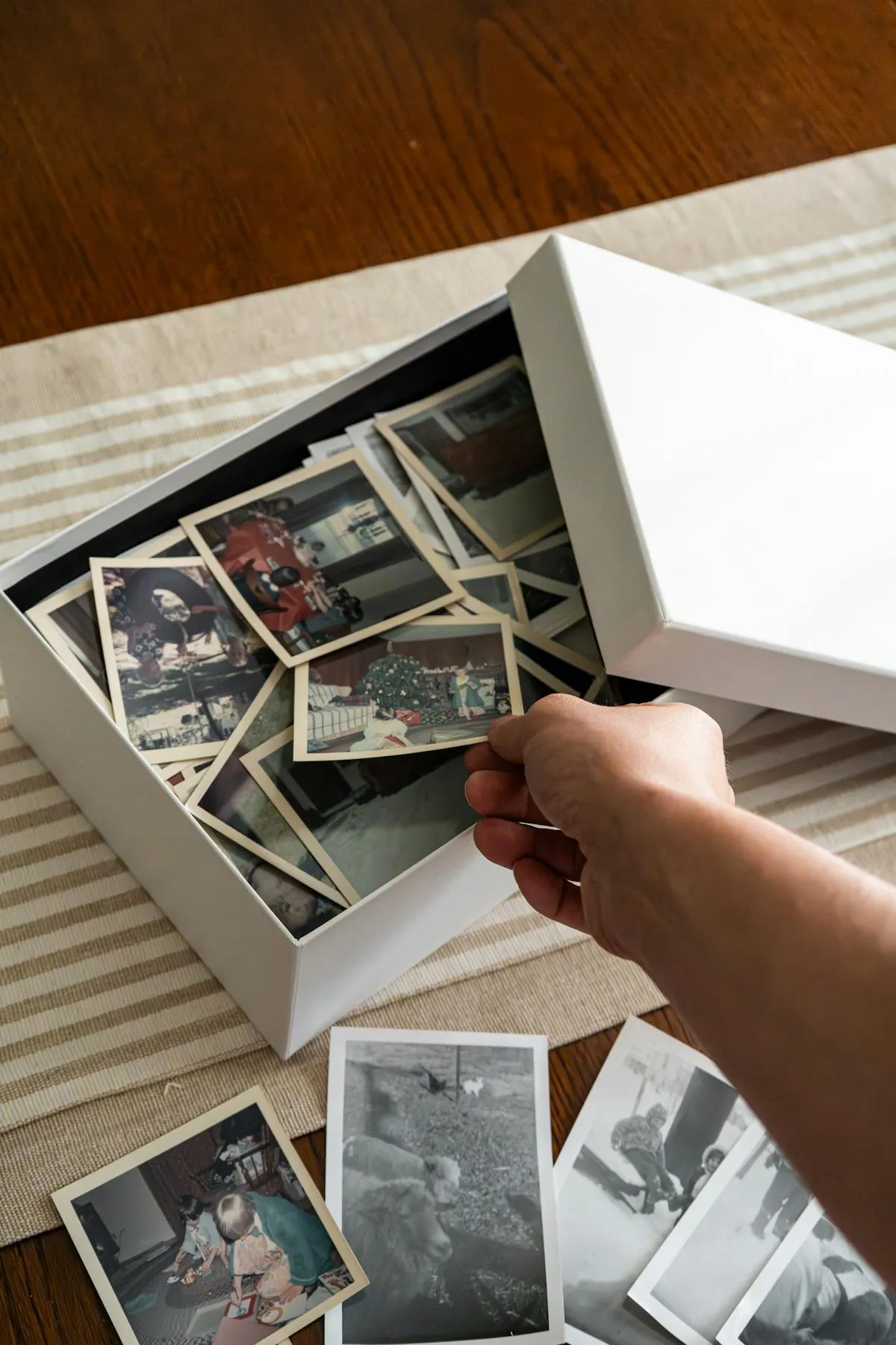 Une main triant une boîte de vieilles photographies de famille, choisissant la photo parfaite pour un portrait commémoratif